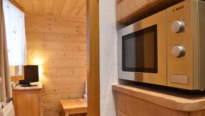 Una cocina compacta con un microondas Bosch, armarios de madera, una pequeña mesa de madera y un televisor sobre un soporte de madera.