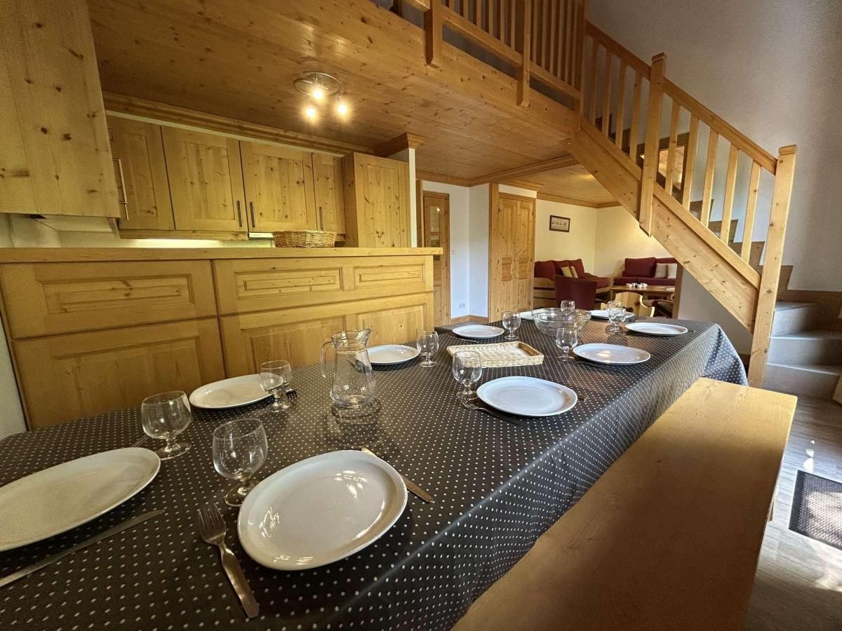 Un coin repas avec une longue table dressée pour six personnes, des meubles en bois et un escalier.