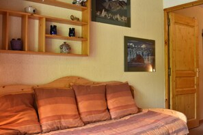 A cozy bedroom with a wooden bed, a shelf with decorative items, and two framed pictures on the wall. - 20m from resort center, 3rd floor, balcony, tv, 24m², Méribel (Méribel - Les Allues)