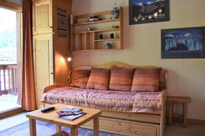 A cozy room with a wooden bed, a small table with books, and a shelf with decorative items. - 150m from ski slopes, 3rd floor, balcony, tv, 24m², Méribel (Méribel - Les Allues)