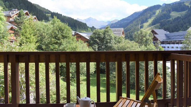 Une terrasse en bois offrant une vue sur un paysage montagneux, avec des maisons et des arbres.