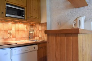 A kitchen with wooden cabinets, a microwave, a sink, and a dishwasher. - 20m from resort center, 3rd floor, balcony, tv, 24m², Méribel (Méribel - Les Allues)