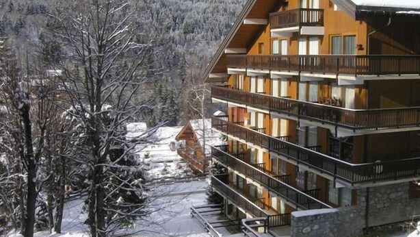 A multi-story wooden building with balconies, surrounded by snow-covered trees and mountains. - 150m from resort center, 4th floor, balcony, ski locker, 26m², Méribel (Méribel - Les Allues)
