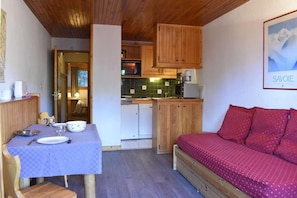 A compact room with a dining table set for two, a kitchenette with wooden cabinets, and a bed with red bedding. - 200m from shops, 1st floor, ski locker, 28m², Méribel (Méribel - Les Allues)
