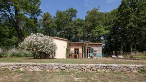 Ein rustikales Haus mit einer Steinsicht im Vordergrund, ein Garten mit einem üppigen Busch und zwei Liegestühle im Hintergrund.