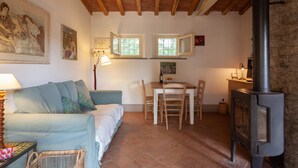 Ein gemütliches Zimmer mit Holzbalkendecke, einer Couch, einem Esstisch mit Stühlen, einem Kamin und Kunstwerken an den Wänden.
