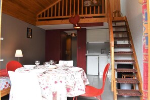 A dining area with a table set for four, a red chair, a small refrigerator, and a wooden staircase. - 20m from resort center, 6th floor, balcony, tv, 31m², Méribel (Méribel - Les Allues)