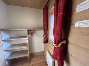 Une pièce avec une étagère en bois à claire-voie, une fenêtre avec des rideaux rouges et un radiateur blanc.