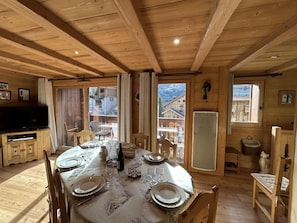 Ein Holzinterieur mit einem Esstisch für vier Personen, einem Fernseher und Blick ins Freie.