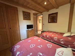 Ein Zimmer mit zwei Betten, einem Holzschrank, einem Fernseher auf einer Kommode und einem Spiegel an der Wand.
