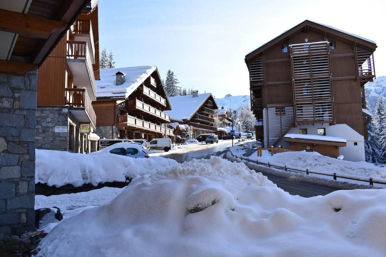 A snow-covered street with wooden buildings, a stone wall, and a clear sky.