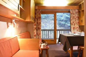 Een gezellig cabin interieur met houten details, een bank, een eettafel gedekt voor twee personen en uitzicht op het bos door de glazen deur.