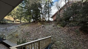 A wooden deck with a stone wall, surrounded by trees and a building in the background.