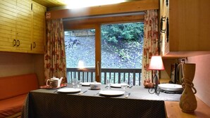 A dining area with a table set for four, a bench, and a view of a forested area through a window.