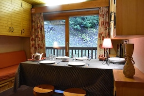 A dining area with a table set for four, a bench, and a view of a forested area through a window.