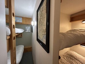 Een smalle gang met stapelbedden aan beide zijden, een inlijst kaart aan de muur en een klein plankje met een ingelijst foto.