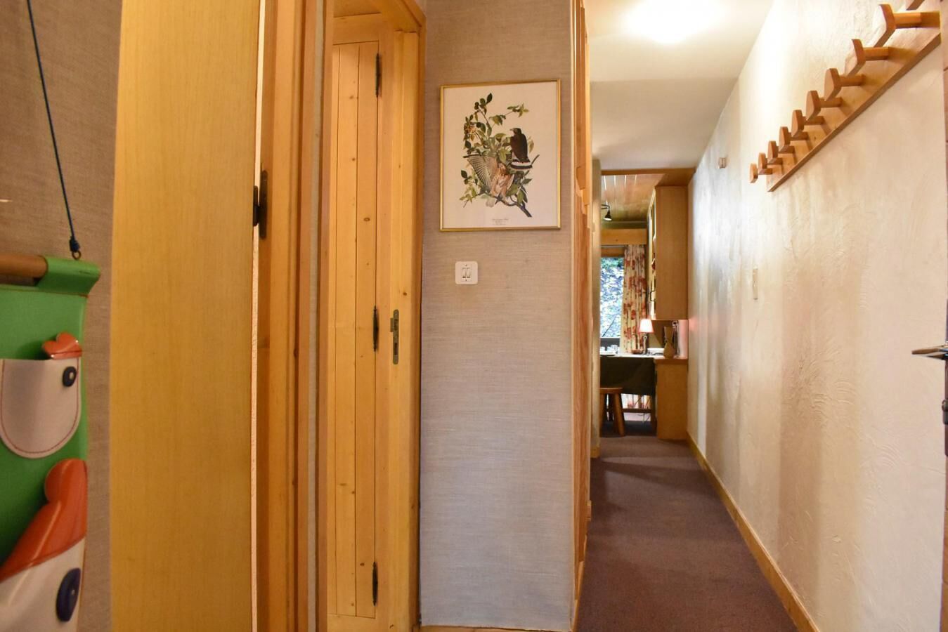 A narrow hallway with wooden doors and a framed botanical illustration on the wall.