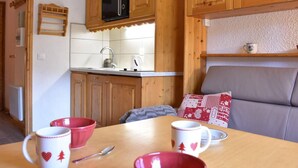 A cozy kitchen with wooden cabinets, a microwave, and a sink. There is a dining table with red and white mugs and a spoon. - 300m from shops, 2nd floor, balcony, tv, ski locker, 18m², Méribel (Méribel - Les Allues)
