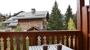 A wooden balcony with a table and two cups, overlooking a forested area with traditional wooden houses. - 300m from shops, 2nd floor, balcony, tv, ski locker, 18m², Méribel (Méribel - Les Allues)