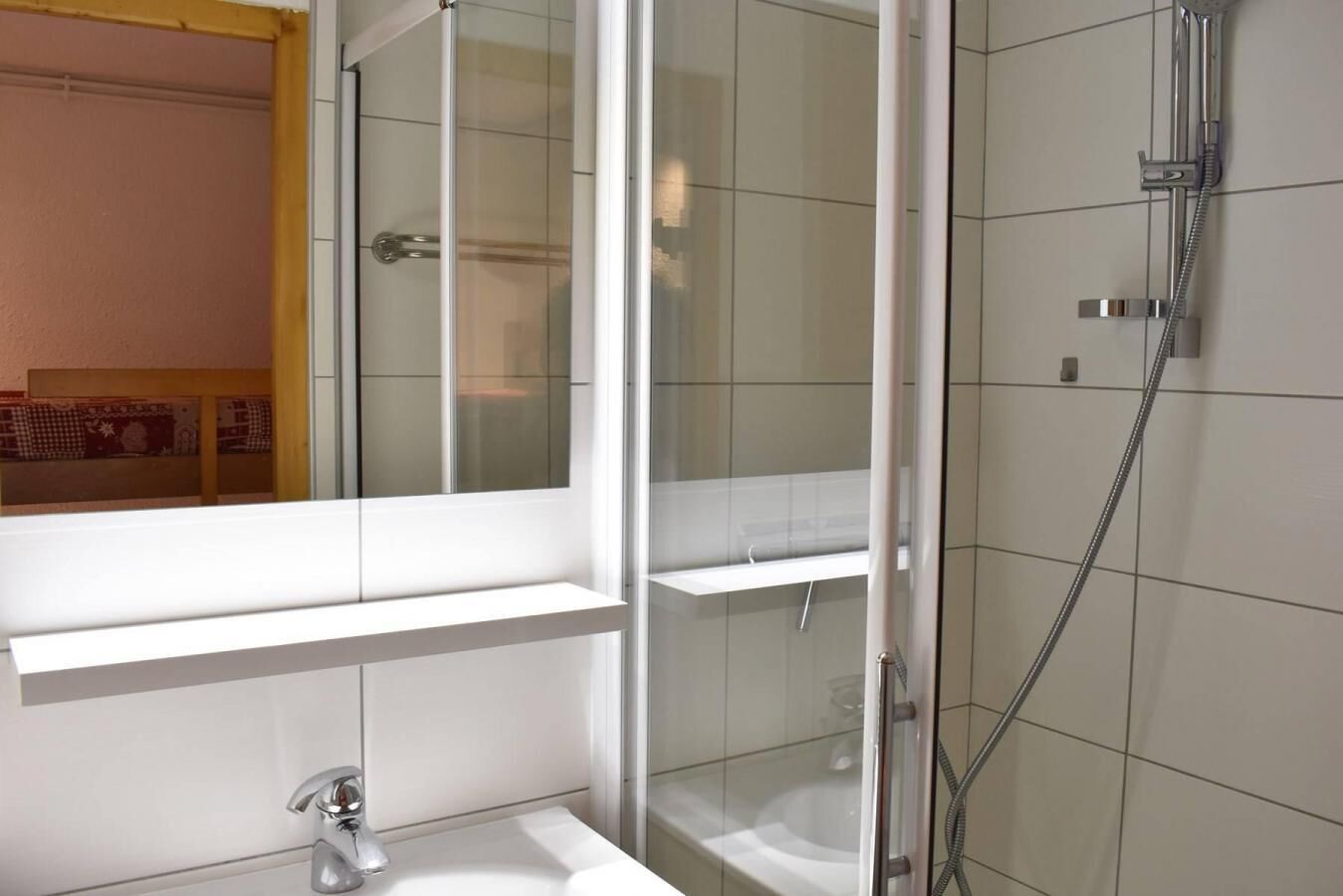 Une salle de bain moderne avec une douche à parois de verre, un lavabo blanc et un miroir au-dessus du lavabo.