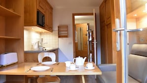 Una cocina funcional con armarios de madera, microondas, cafetera y una mesa de comedor con platos, tazas y tetera.