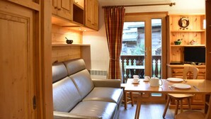 Una habitación acogedora con sofá, una mesa de comedor con sillas, armarios de madera y televisor.