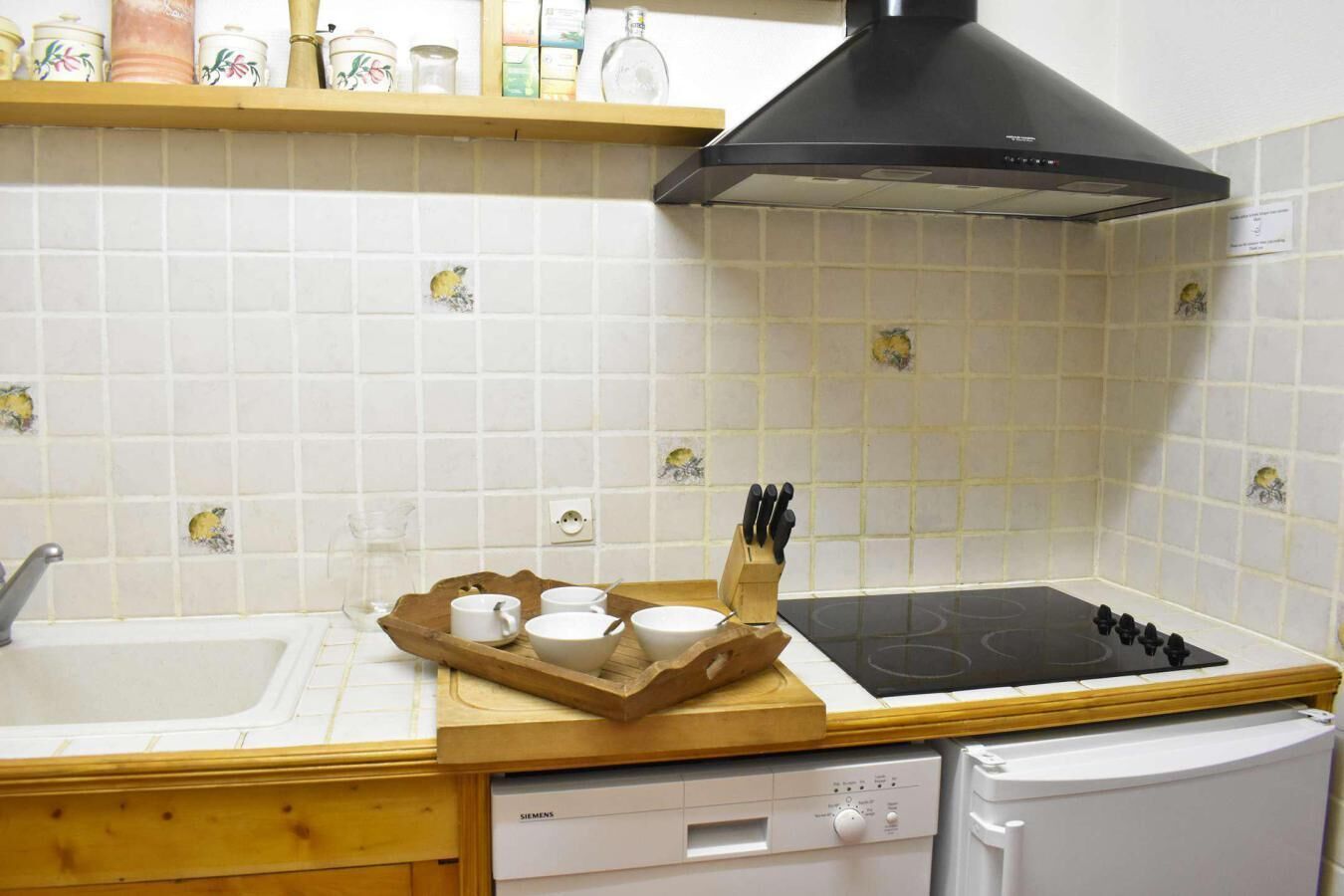 Una cucina con piastrelle bianche, una cappa aspirante nera, una lavastoviglie Siemens e un vassoio di legno con tazze e un portacoltelli.