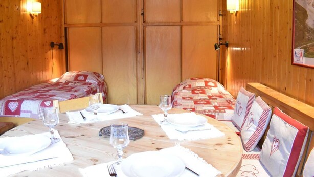 Una habitación acogedora de madera con dos camas, una mesa de comedor preparada para dos personas y un cuadro en la pared.