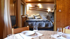 Una habitación acogedora de madera con una cama, un televisor y una mesa de comedor preparada para dos personas.