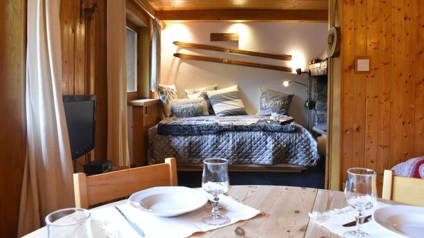 Una stanza accogliente in legno con un letto, una televisione e un tavolo da pranzo per due persone.