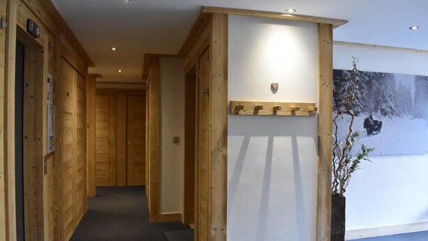 Un couloir en bois avec un porte-manteau, une porte et une œuvre d’art accrochée au mur.