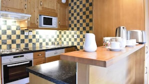 Une cuisine compacte avec des meubles en bois, un four à micro-ondes, une cuisinière et un dosseret à carreaux.