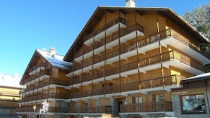 Un bâtiment en bois à plusieurs étages, doté de balcons, qui ressemble probablement à un hôtel ou à un chalet, avec plusieurs voitures garées devant.