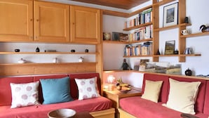 Un salon chaleureux avec un canapé rouge, une table basse en bois et une bibliothèque remplie de livres et d’objets décoratifs.