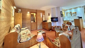 A cozy living room with wooden walls and furniture, a television, and a small kitchen area. - 200m from ski slopes, 6th floor, swimming pool, tv, ski locker, 50m², Méribel (Méribel - Les Allues)
