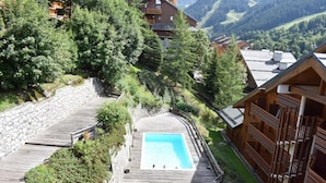 A wooden deck with a swimming pool, surrounded by stone walls and lush greenery. - 200m from ski slopes, 6th floor, swimming pool, tv, ski locker, 50m², Méribel (Méribel - Les Allues)