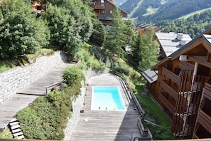 A wooden deck with a swimming pool, surrounded by stone walls and lush greenery.