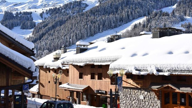 A snow-covered mountain village with wooden buildings and a clear view of the mountains in the background.