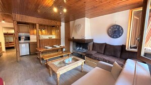 A cozy interior with a wooden ceiling, a dining area with benches, a sofa, and a fireplace.