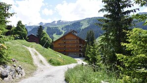 A wooden lodge with a balcony, surrounded by lush greenery and mountains in the background. - Ski-in/ski-out & foot of the slopes, balcony, tv, ski locker, 105m², Méribel (Méribel - Les Allues)