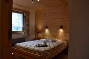 A bedroom with a wooden headboard, a bed with floral bedding, a nightstand with a lamp, and a window with patterned curtains. - 100m from resort center, balcony, tv, ski locker, 105m², Méribel (Méribel - Les Allues)