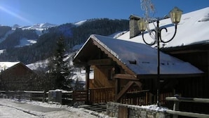 A wooden chalet with a snow-covered roof, a stone wall, and a metal fence. - 100m from resort center, 2nd floor, tv, 24m², Méribel (Méribel - Les Allues)