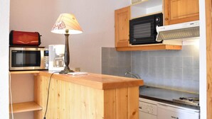 A compact kitchen with wooden cabinets, a microwave, a coffee maker, and a gas stove. - 100m from resort center, 2nd floor, tv, 24m², Méribel (Méribel - Les Allues)