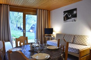 A cozy room with a wooden ceiling, a dining table set with plates and glasses, a sofa with patterned cushions, and a television on a stand. - 300m from ski slopes, 1st floor, terrace, tv, 25m², Méribel (Méribel - Les Allues)