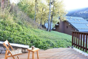 A wooden deck with a chair and a table, overlooking a grassy area with trees and a building with solar panels. - 300m from ski slopes, 1st floor, terrace, tv, 25m², Méribel (Méribel - Les Allues)