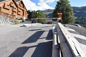 A mountain road with a wooden guardrail, a building with balconies, and a view of the mountains. - 300m from ski slopes, 1st floor, terrace, tv, 25m², Méribel (Méribel - Les Allues)