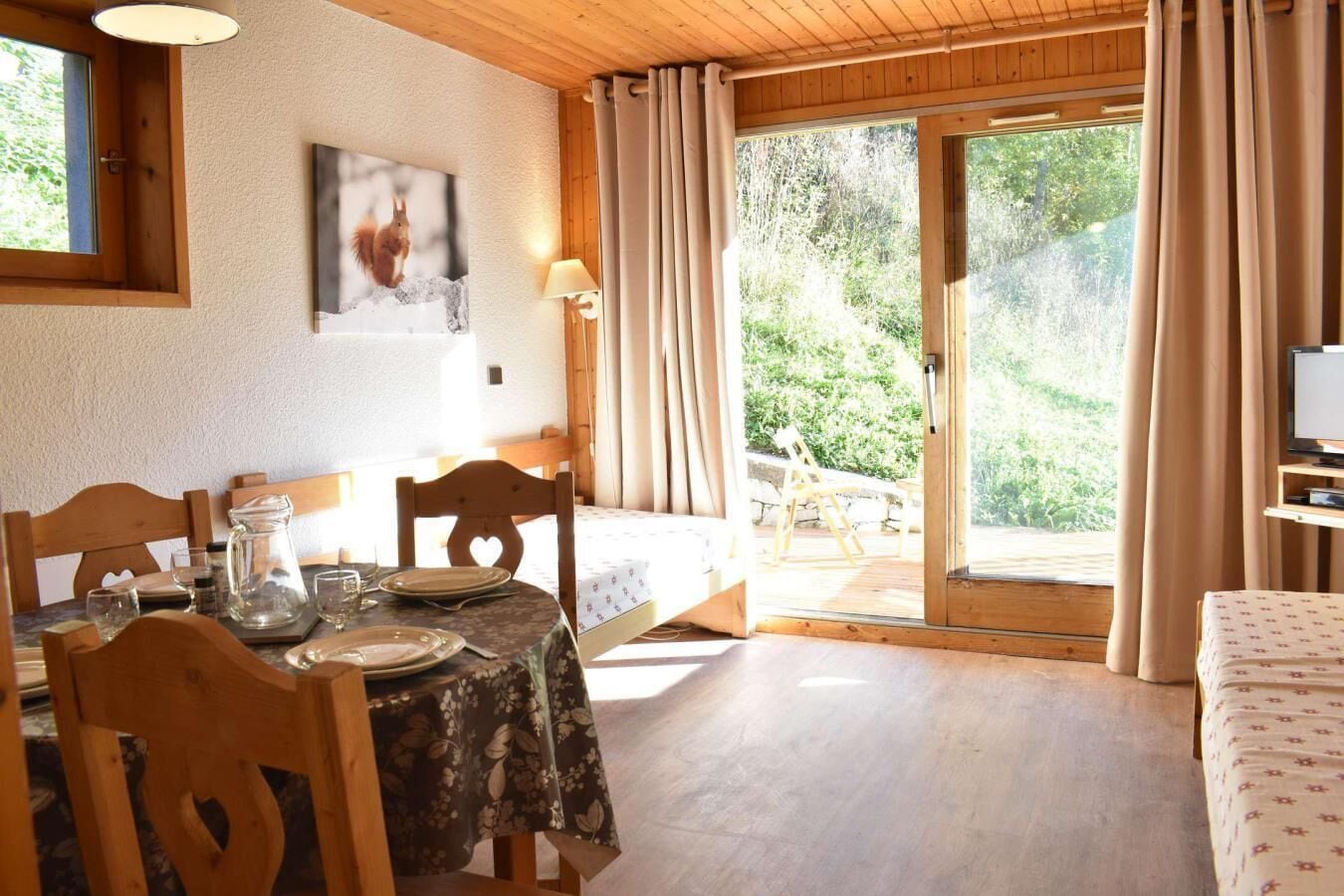 Comedor con una mesa dispuesta para dos, un banco de madera y vistas al exterior a través de un ventanal.