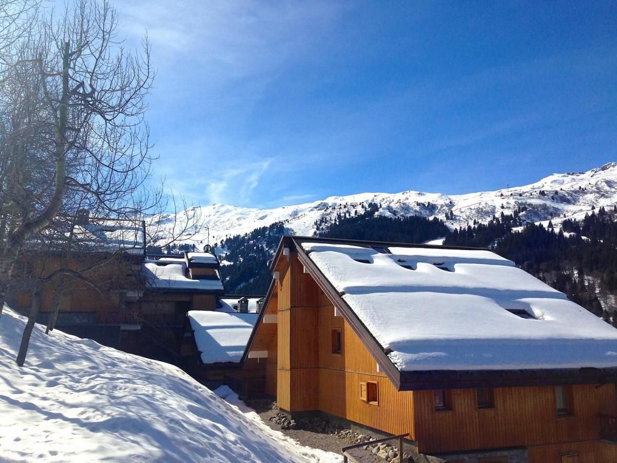 A wooden chalet with a sloped roof, surrounded by snow-covered mountains and a clear sky.