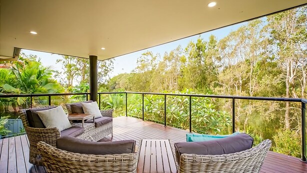 A balcony with wicker furniture, a glass barrier, and a view of dense greenery.