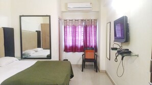Habitació d'hotel amb un llit, una cadira, una taula amb un telèfon, una televisió, un mirall i una finestra amb cortines.